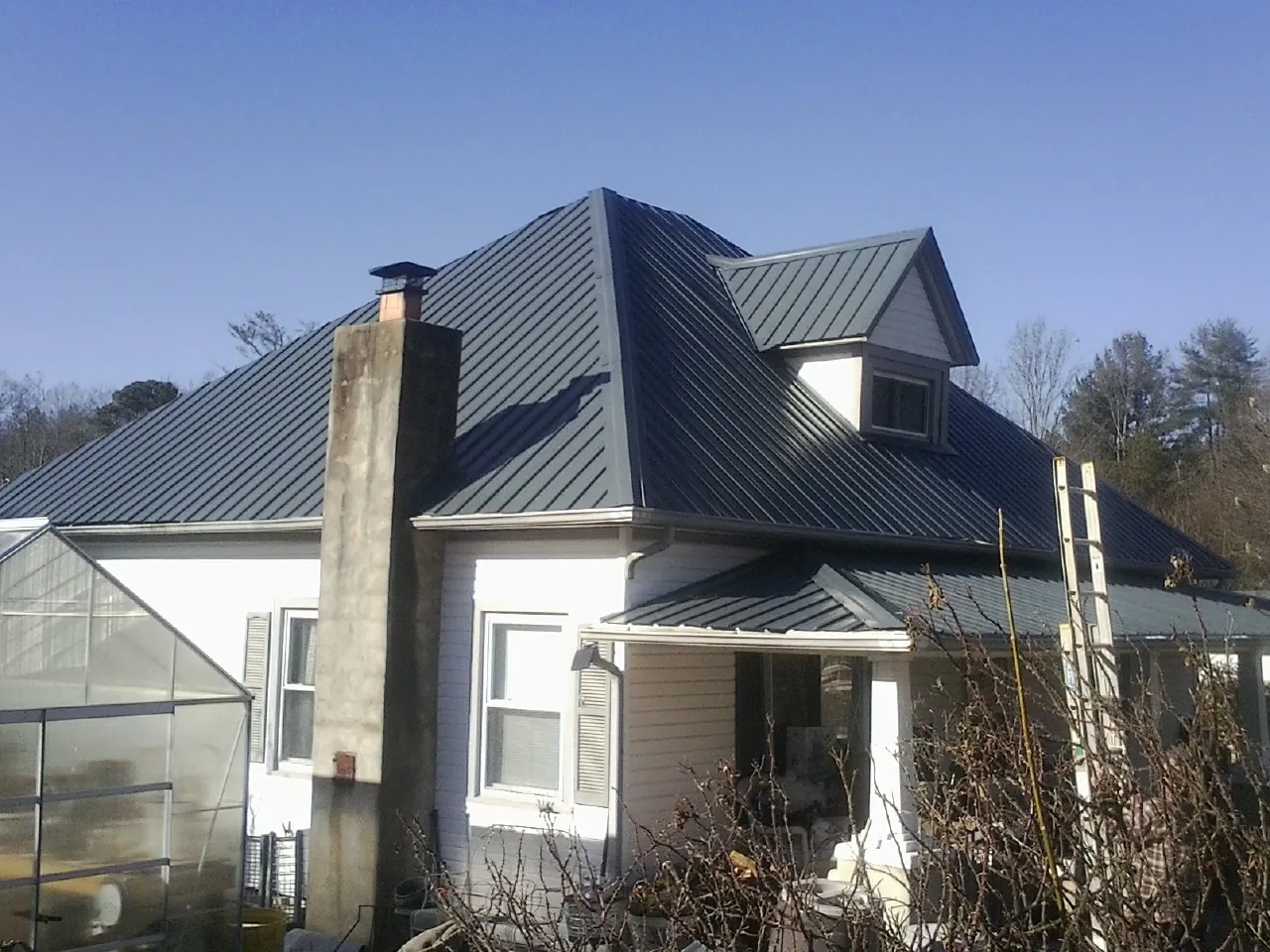 Dark blue standing seam metal roof on a white farmhouse with dormer — Slate & Tile Roof Repair by Roofing Brothers in Giddings