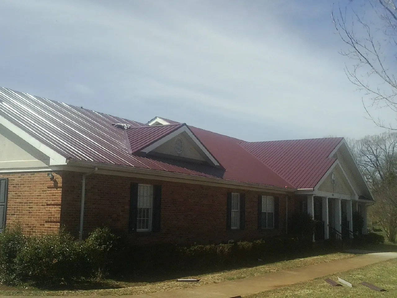 Red metal roof with gabled entries on a long brick building, from a Hail Damage Roof Repair job in Giddings