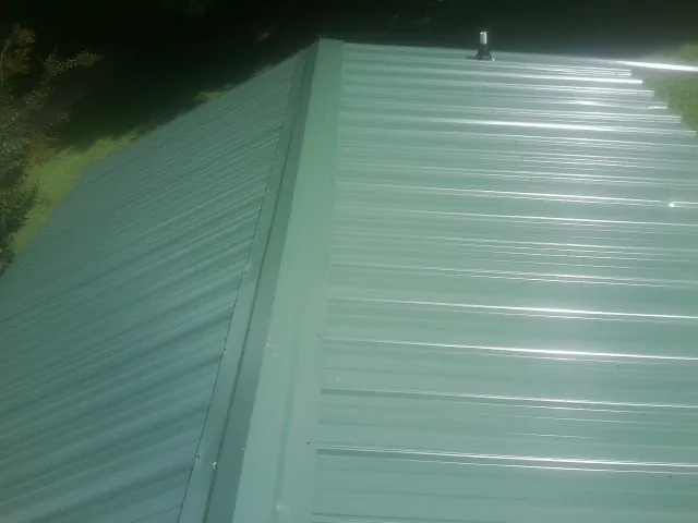 New green metal panels meeting at the ridge of a roof — Flat Roof Repair work by our crew in Giddings