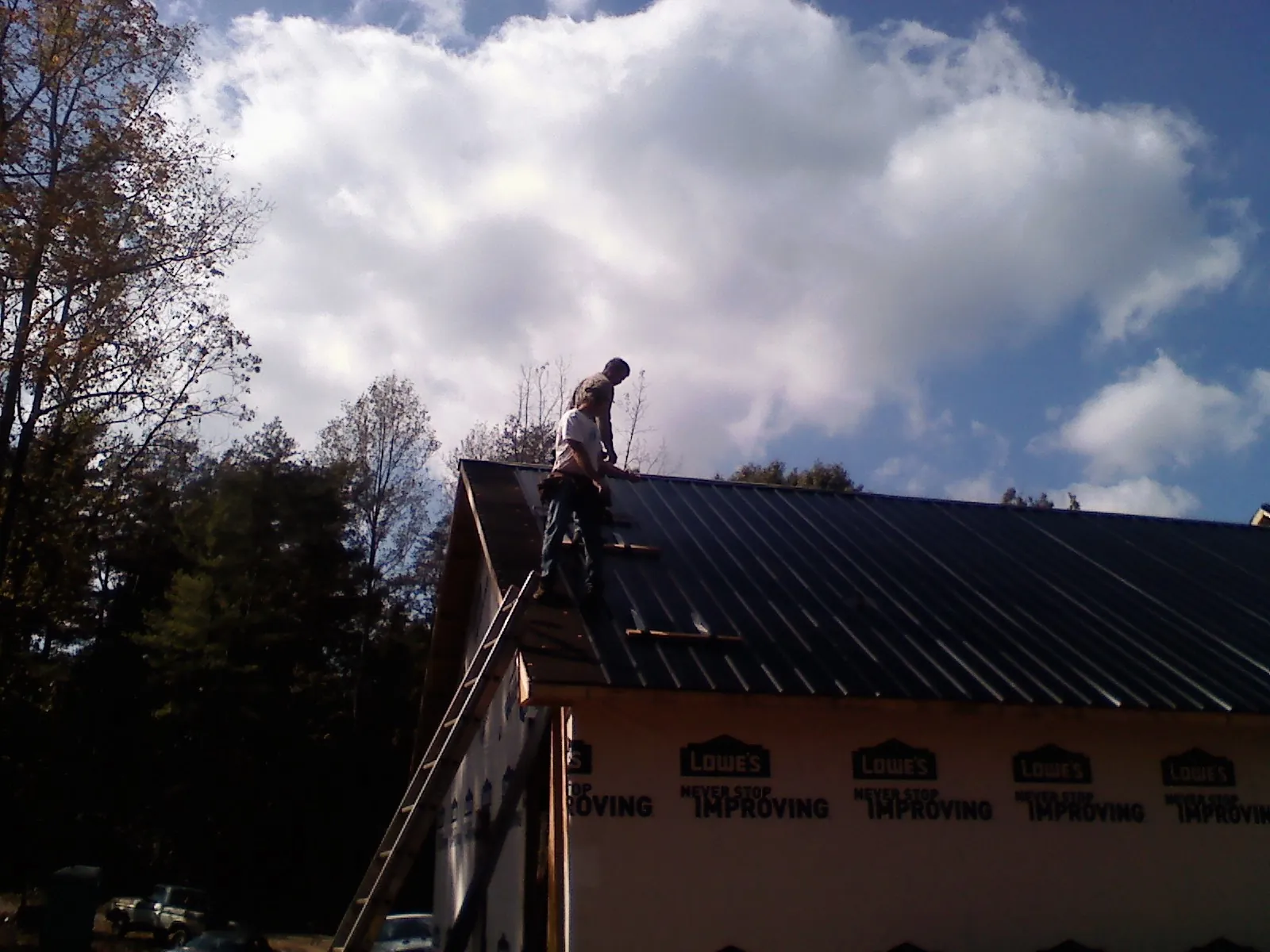 Roofer fastening dark metal panels high against a cloudy sky, from a Roof Inspection job in Giddings