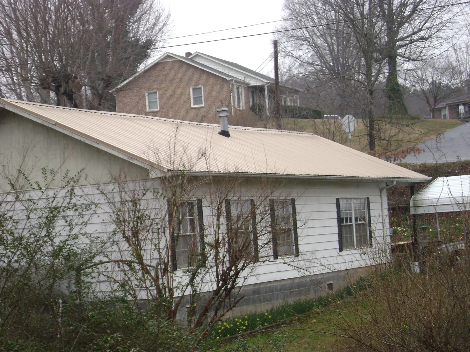 Tan metal roof on a white sided house set into a hillside — Commercial Roofing by Roofing Brothers in Giddings