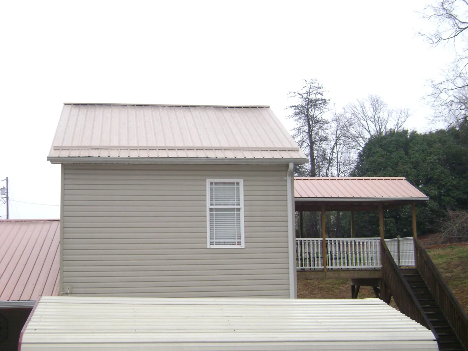 Tan metal roofs on a two story addition and attached porch, from a Roof Replacement job in Giddings